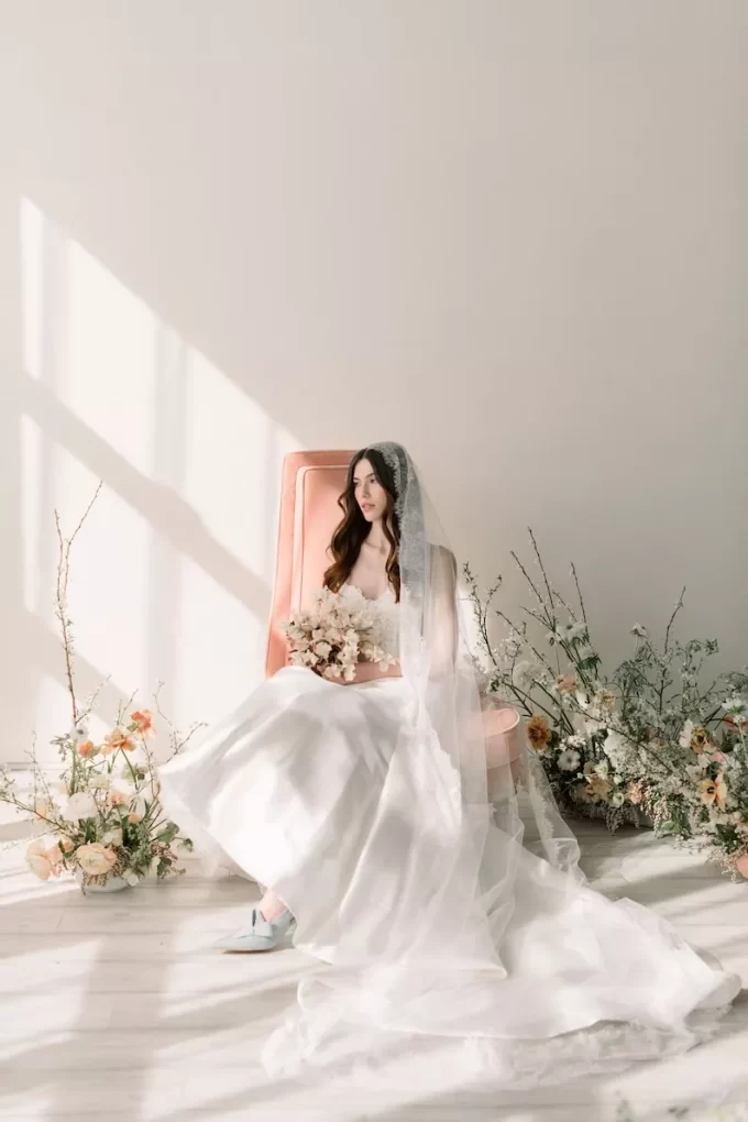 Bride wearing mantilla lace veil and wedding gown sitting in pink chair