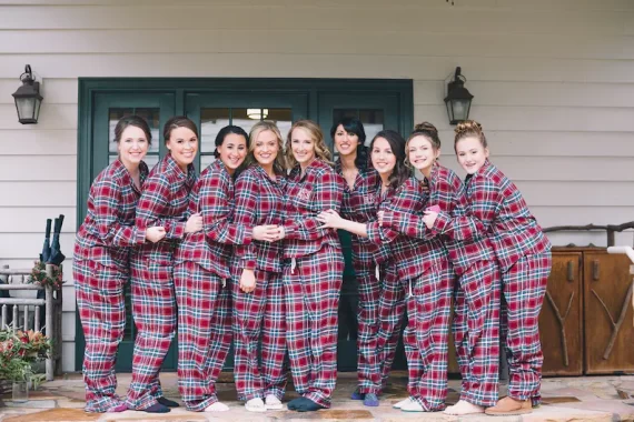 Bridesmaids wearing navy and red striped plaid flannel pajamas standing and smiling together