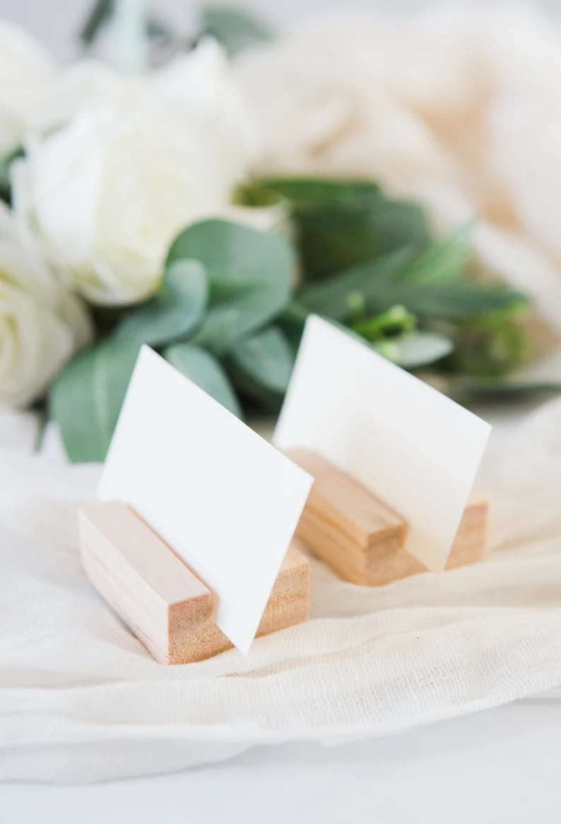 Close-up of a wooden place card holder holding a folded wedding place card