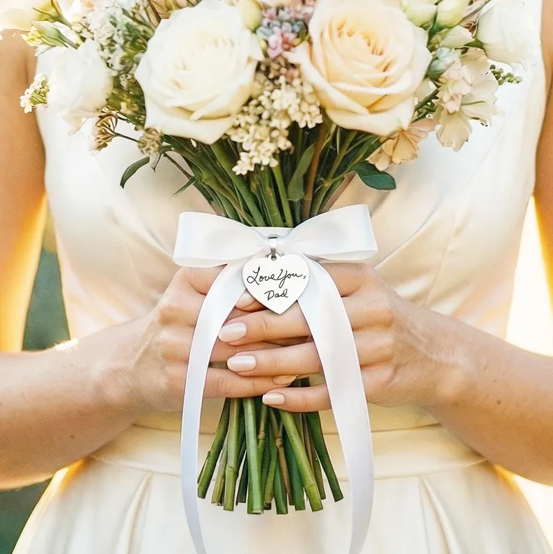 bride holding bouquet with heart charm engraved with handwritten message