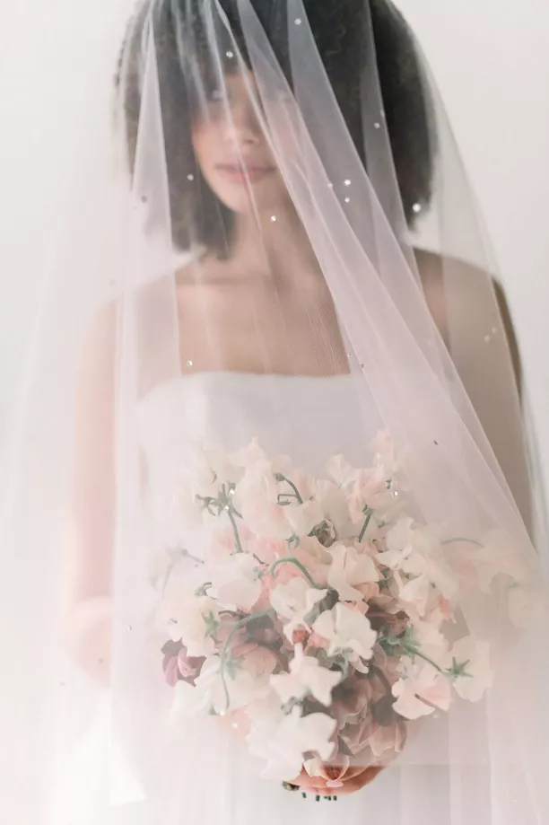 bride covering face with bridal veil featuring pearls