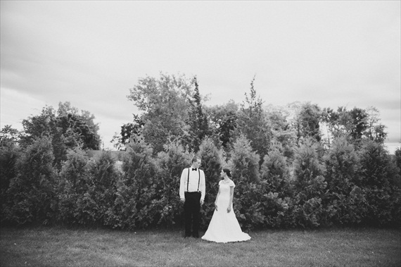 bride and groom - b & w image - standing in front of woods.  groom in suspenders with bow tie - photo: michelle gardella photography