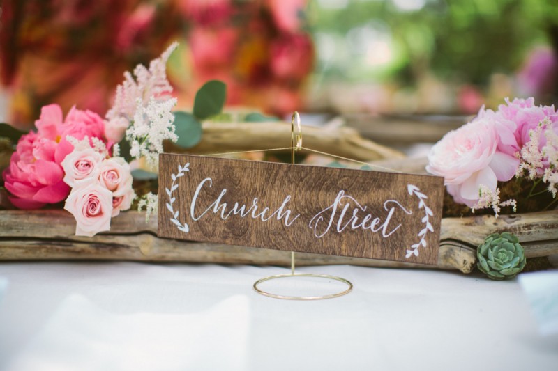 Use table names at your wedding instead of table numbers.  Cute and creative idea!  Sign by Paper and Pine Co. | Photo: Juliet Elizabeth Photography | table names weddings - https://emmalinebride.com/reception/table-names-weddings/