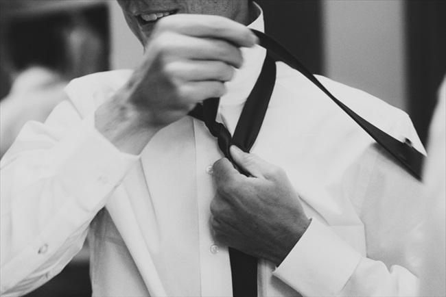The groom putting on his tie | Photo: Searching for the Light Photography LLC | via https://emmalinebride.com/real-weddings/colorado-chic-wedding-kendall-brian/