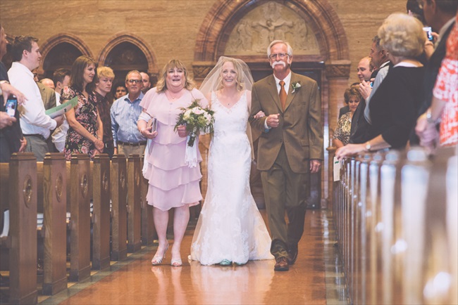 The bride walks down the aisle with her mother and father | Photo: Searching for the Light Photography LLC | via https://emmalinebride.com/real-weddings/colorado-chic-wedding-kendall-brian/