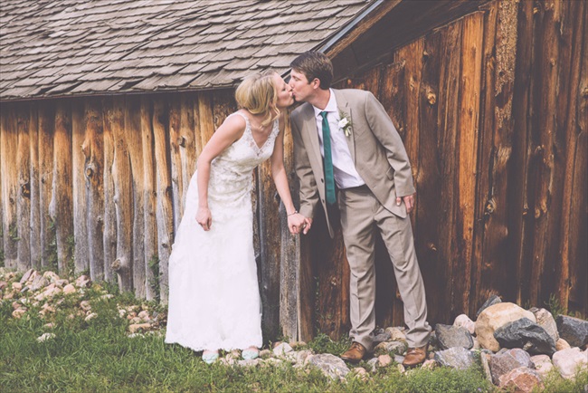 The bride and groom kiss in front of the barn | Photo: Searching for the Light Photography LLC | via https://emmalinebride.com/real-weddings/colorado-chic-wedding-kendall-brian/
