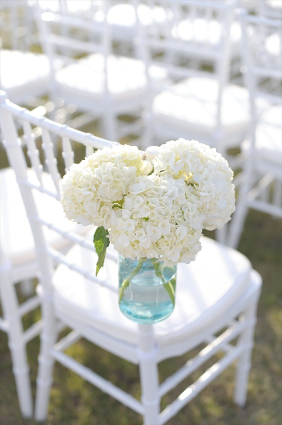 blue mason jars filled with white hydrangea flowers and attached to chairs