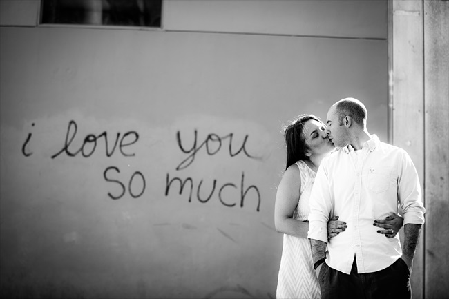 engaged couple kiss by graffiti that says, 