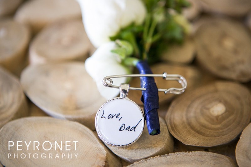 This boutonniere pin features a charm that is handwritten on one side and features a photo on the other. It is used as a way to remember a loved one who has passed at your wedding. | Handmade Wedding Charms via https://emmalinebride.com/decor/handmade-wedding-charms/